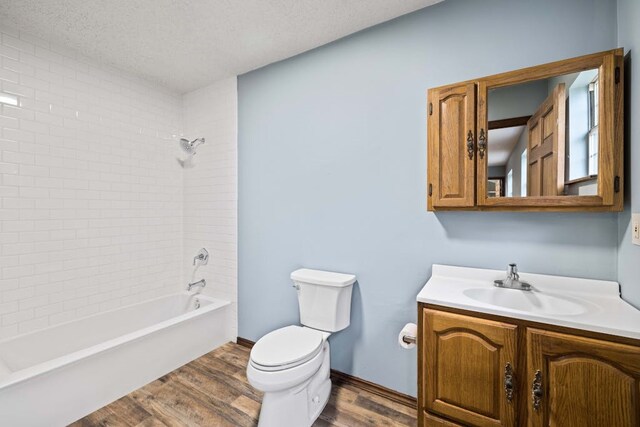 full bathroom featuring a textured ceiling, hardwood / wood-style flooring, toilet, vanity, and tiled shower / bath combo