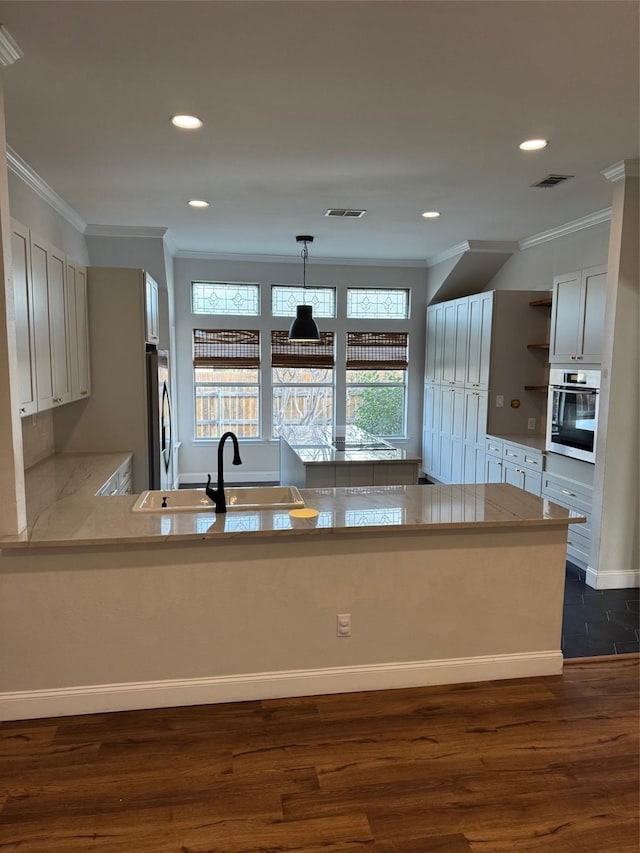 kitchen with stainless steel appliances, sink, decorative light fixtures, kitchen peninsula, and dark wood-type flooring