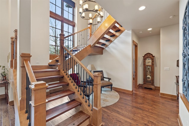 staircase with a towering ceiling, a chandelier, and hardwood / wood-style floors