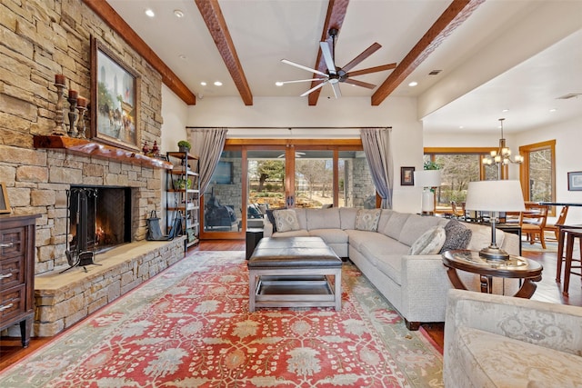 living room with ceiling fan with notable chandelier, beam ceiling, light hardwood / wood-style flooring, and a stone fireplace