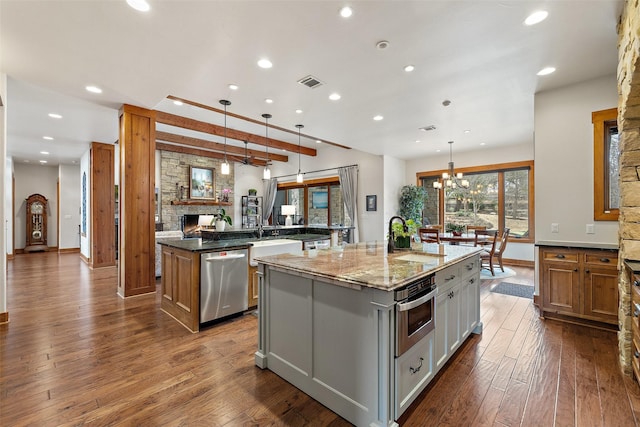 kitchen with light stone counters, an island with sink, stainless steel appliances, and hanging light fixtures