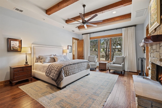 bedroom featuring dark hardwood / wood-style flooring, a fireplace, ceiling fan, and beamed ceiling