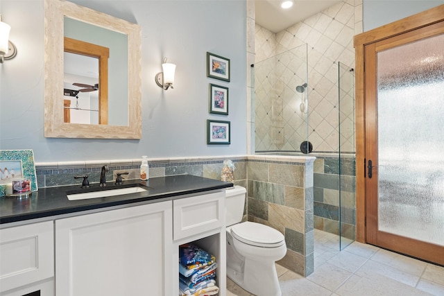 bathroom with tile walls, a shower with door, vanity, and toilet