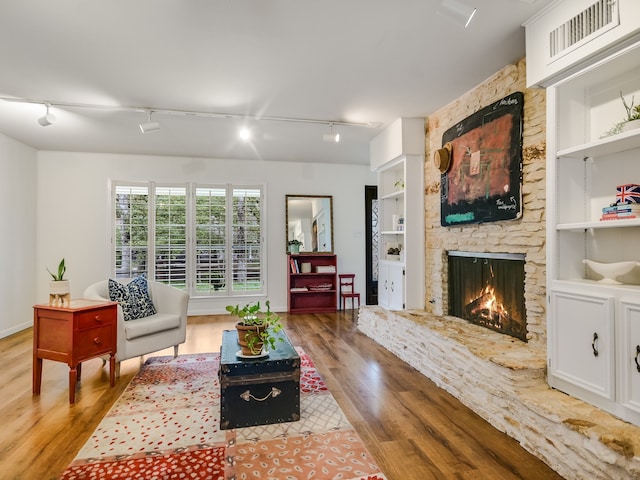 living room with a fireplace, light hardwood / wood-style flooring, built in features, and rail lighting