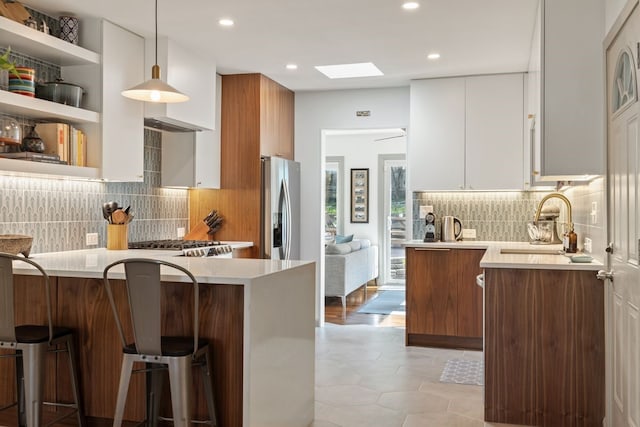 kitchen with stainless steel appliances, a skylight, kitchen peninsula, white cabinets, and decorative light fixtures