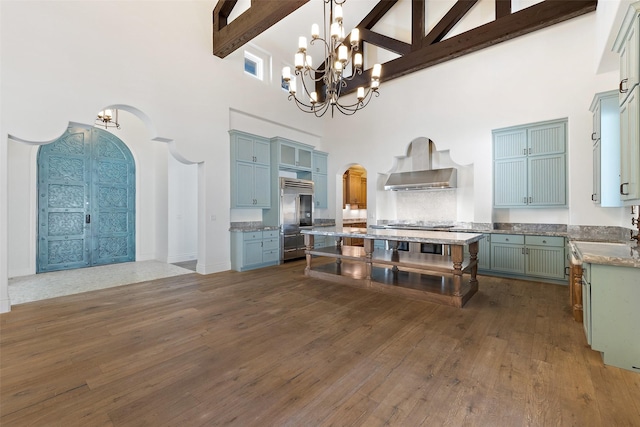 kitchen featuring a high ceiling, wall chimney exhaust hood, stainless steel built in fridge, and beamed ceiling