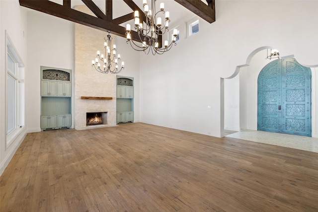 unfurnished living room featuring a high ceiling, hardwood / wood-style flooring, beamed ceiling, and a stone fireplace