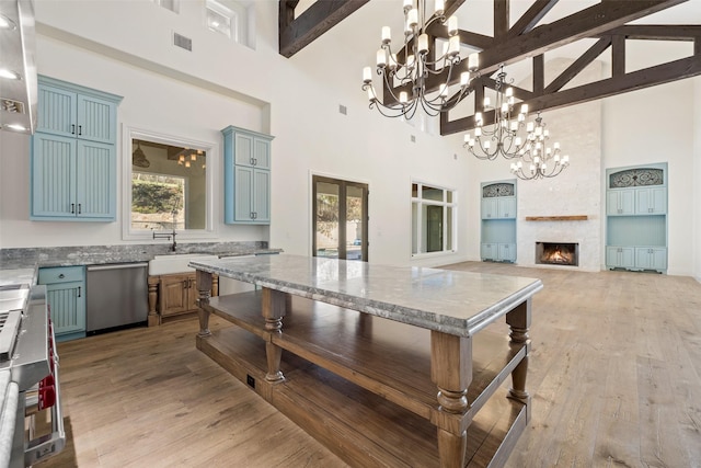 kitchen featuring a large fireplace, pendant lighting, stainless steel dishwasher, and high vaulted ceiling