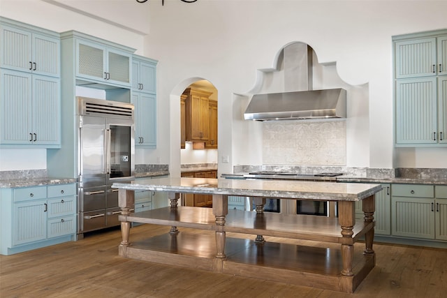 kitchen featuring appliances with stainless steel finishes, dark hardwood / wood-style floors, light stone counters, and wall chimney exhaust hood