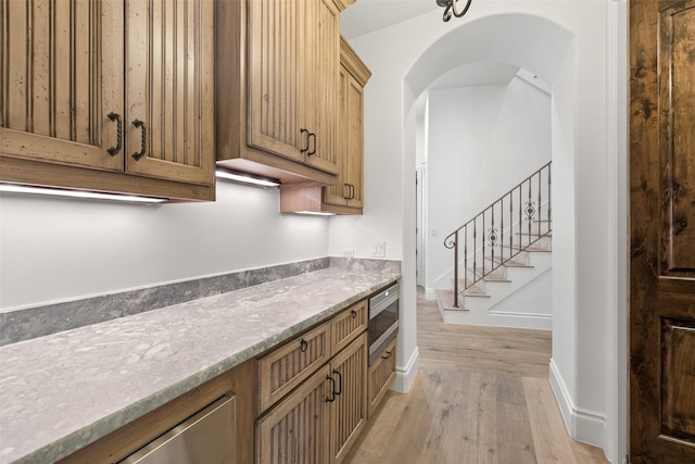 kitchen featuring light stone counters, stainless steel microwave, and light hardwood / wood-style flooring