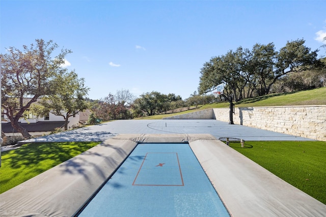 view of pool with a lawn and basketball hoop