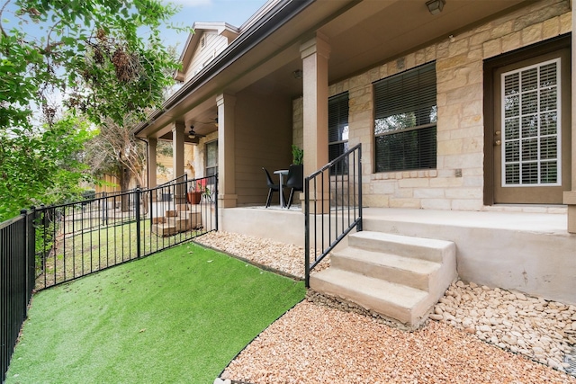 view of exterior entry featuring ceiling fan and a lawn