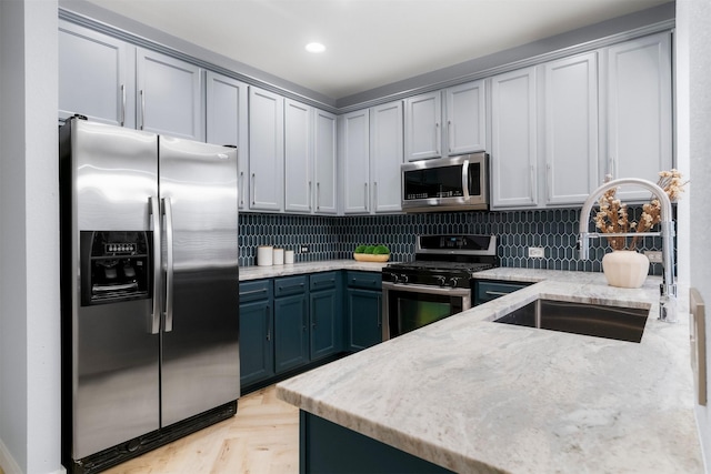 kitchen with light stone countertops, light parquet floors, stainless steel appliances, decorative backsplash, and sink