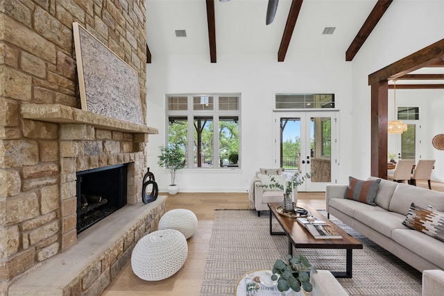 living room with a stone fireplace, french doors, light hardwood / wood-style flooring, high vaulted ceiling, and beam ceiling