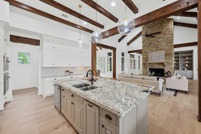 kitchen with a center island with sink, beam ceiling, white cabinetry, backsplash, and sink