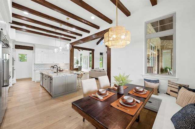 dining space with beam ceiling, a notable chandelier, light wood-type flooring, and sink