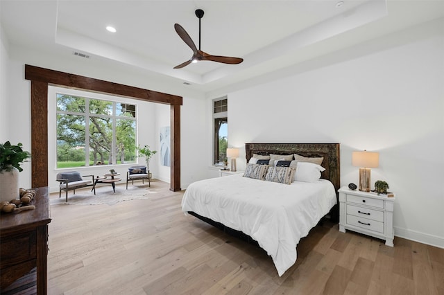 bedroom with light hardwood / wood-style floors, ceiling fan, and a tray ceiling