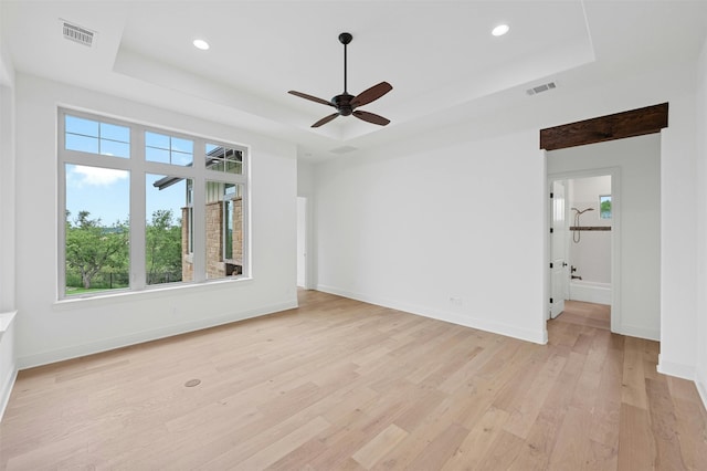 empty room with ceiling fan, a tray ceiling, and light hardwood / wood-style flooring