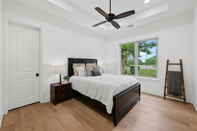 bedroom featuring light wood-type flooring, ceiling fan, and a tray ceiling