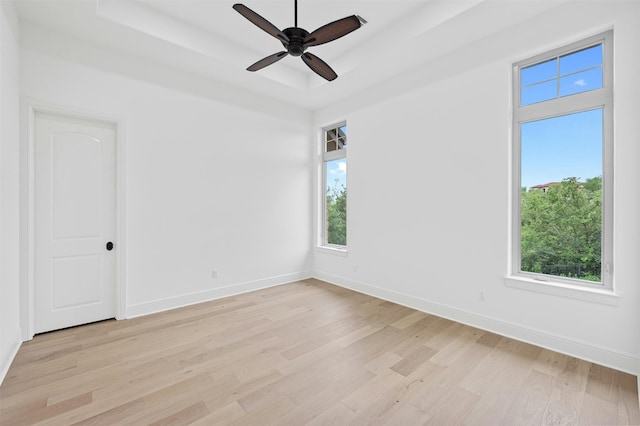 unfurnished room featuring a raised ceiling, ceiling fan, and light hardwood / wood-style flooring