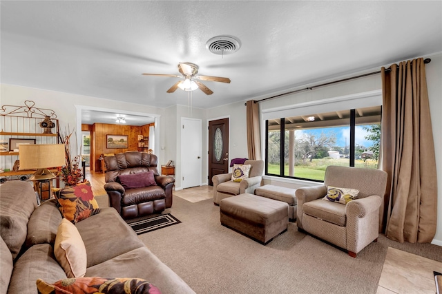 living room featuring ceiling fan, wooden walls, and light carpet