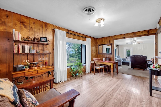 living room featuring wooden walls, ceiling fan, and light hardwood / wood-style flooring