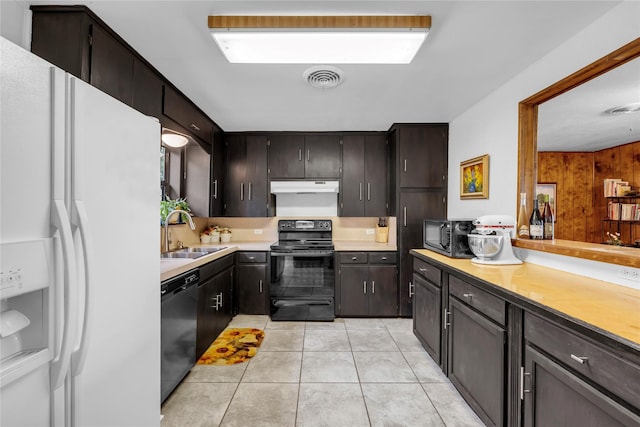 kitchen with sink, light tile patterned floors, wood walls, dark brown cabinets, and black appliances