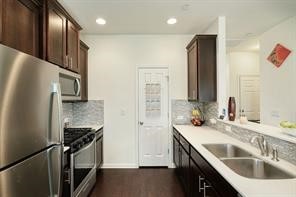 kitchen featuring stainless steel appliances, sink, tasteful backsplash, dark brown cabinets, and dark wood-type flooring