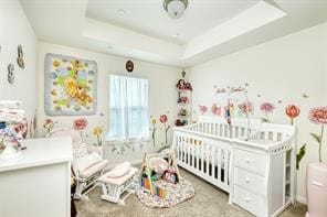 bedroom featuring a nursery area and a tray ceiling