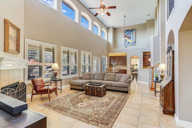 tiled living room with a tiled fireplace, a high ceiling, and ceiling fan