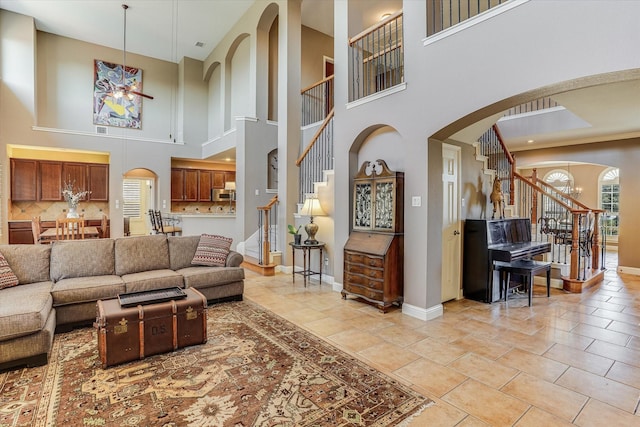 living room with a towering ceiling, ceiling fan with notable chandelier, and light tile patterned floors