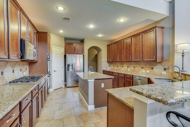 kitchen with appliances with stainless steel finishes, a kitchen bar, sink, light stone counters, and a center island with sink