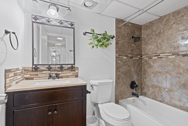 full bathroom with toilet, a drop ceiling, decorative backsplash, tiled shower / bath, and vanity