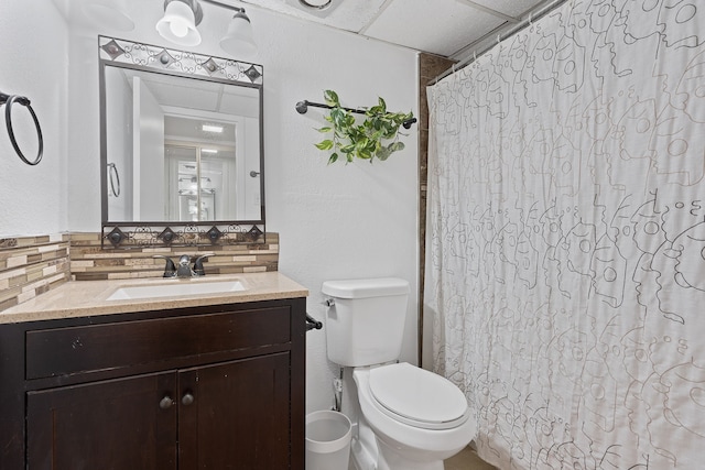 bathroom featuring toilet, vanity, decorative backsplash, and a drop ceiling