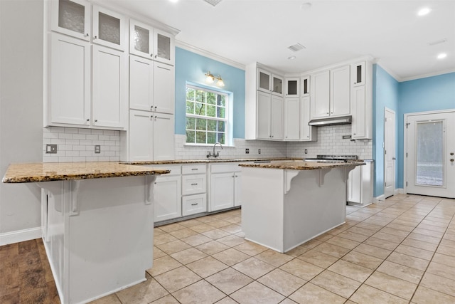 kitchen featuring light stone counters, a kitchen island, white cabinetry, and a breakfast bar area