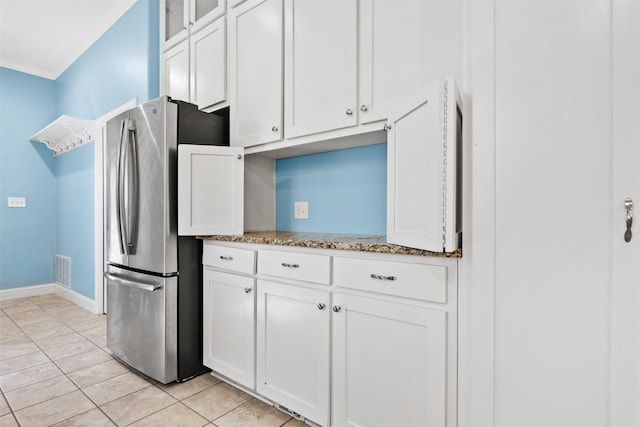 kitchen featuring white cabinets, light tile patterned flooring, light stone countertops, and stainless steel refrigerator