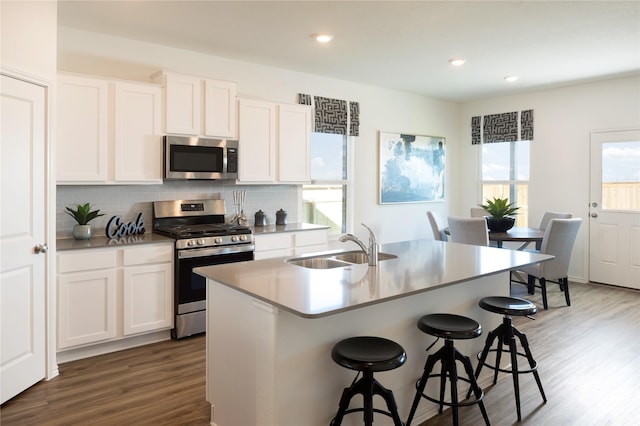 kitchen with stainless steel appliances, a center island with sink, dark hardwood / wood-style flooring, and white cabinetry