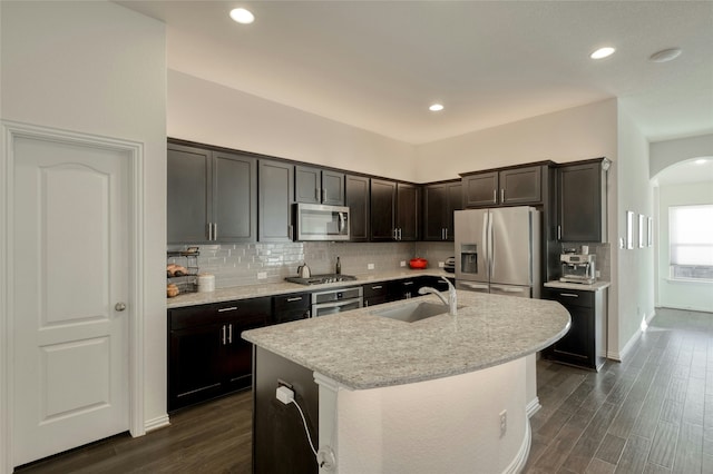 kitchen featuring dark wood-type flooring, sink, a center island with sink, appliances with stainless steel finishes, and dark brown cabinetry