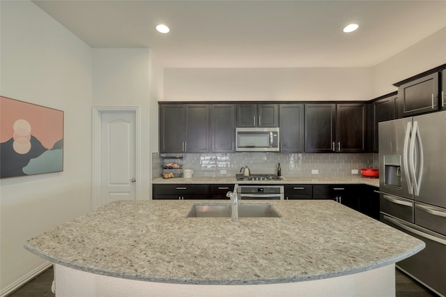 kitchen with stainless steel appliances, a center island with sink, tasteful backsplash, and light stone counters