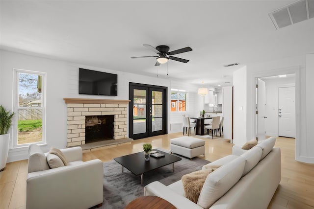 living room featuring ceiling fan, light hardwood / wood-style flooring, plenty of natural light, and a brick fireplace