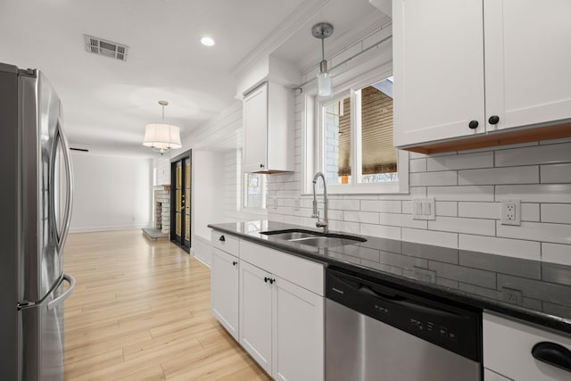 kitchen featuring appliances with stainless steel finishes, white cabinets, decorative light fixtures, and sink