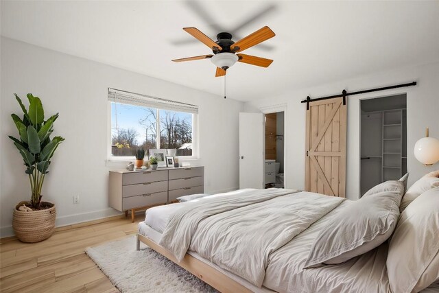 bedroom featuring a walk in closet, light hardwood / wood-style floors, a closet, ceiling fan, and a barn door