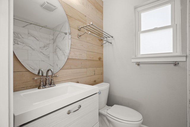 bathroom with toilet, vanity, plenty of natural light, and wooden walls