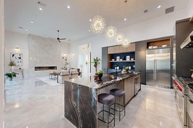 kitchen with a kitchen bar, a kitchen island, built in fridge, a fireplace, and dark stone counters