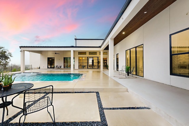 pool at dusk with a patio area and ceiling fan