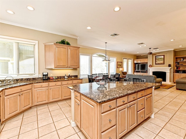 kitchen with hanging light fixtures, light tile patterned floors, dark stone counters, light brown cabinetry, and sink