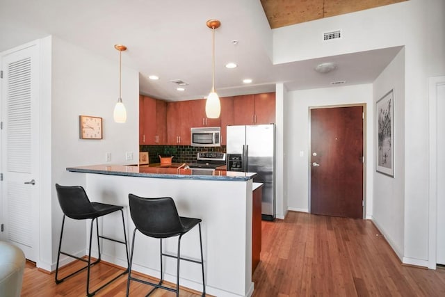 360 Nueces St Unit 1318, Austin, TX 78701 - kitchen featuring appliances with stainless steel finishes, a peninsula, backsplash, brown cabinets, and light wood-type flooring