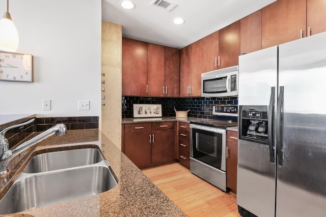 kitchen featuring sink, tasteful backsplash, decorative light fixtures, dark stone countertops, and appliances with stainless steel finishes