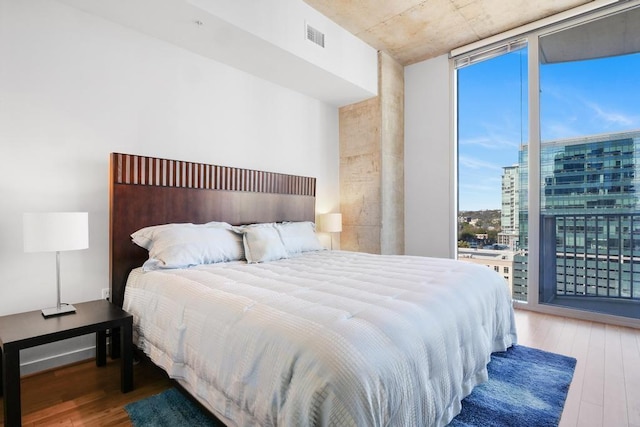 bedroom with access to outside, wood-type flooring, and a wall of windows