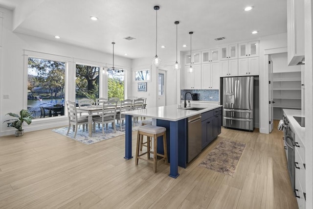 kitchen featuring a kitchen island with sink, appliances with stainless steel finishes, sink, white cabinetry, and decorative light fixtures